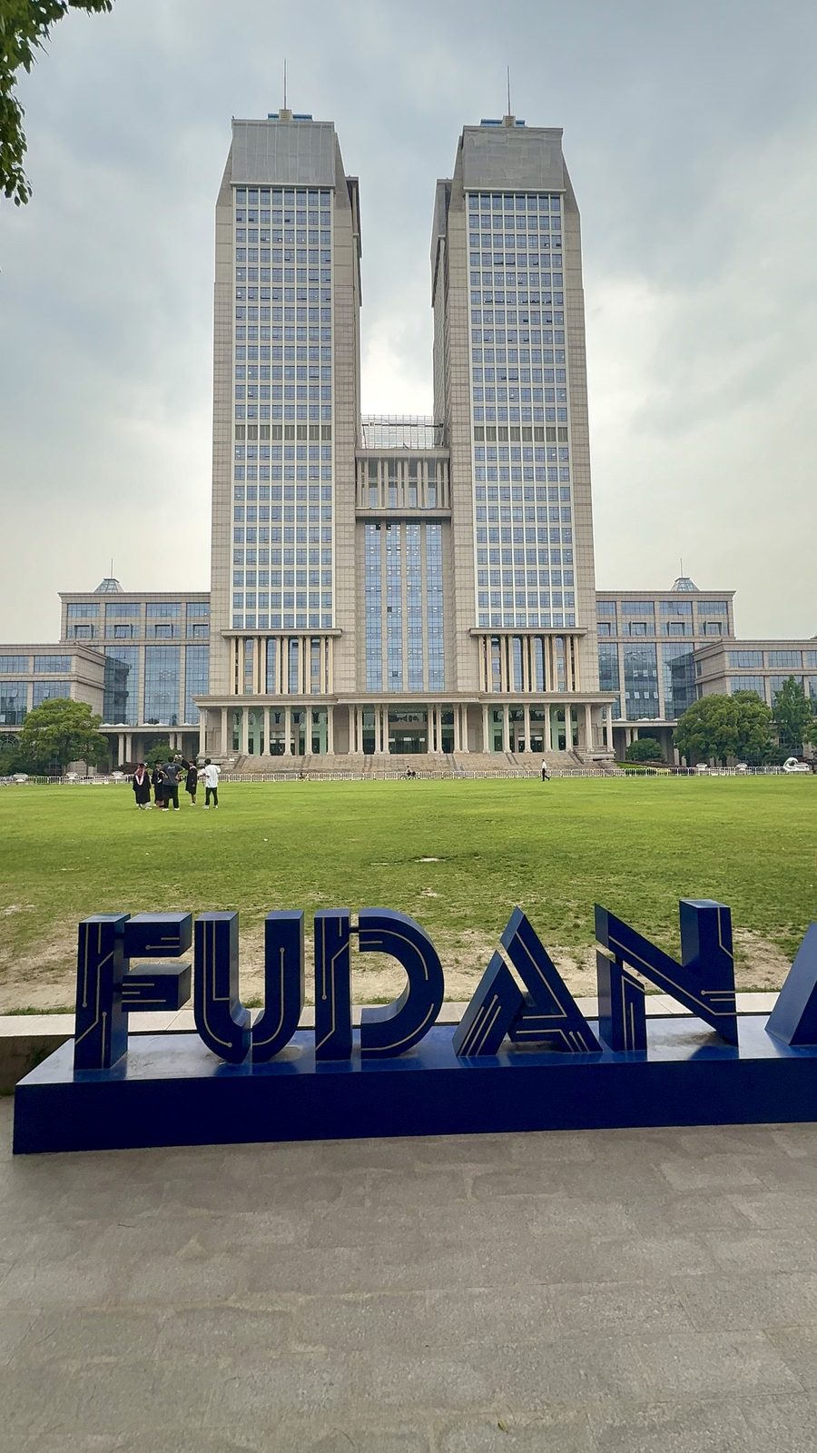 Guanghua twin towers at Fudan University, graduates on the lawn behind the FUDAN sign